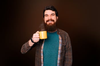Homem sorridente com barba bebe uma xícara amarela de café Café Pelé