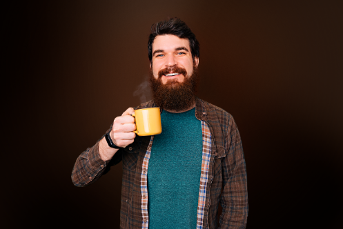 Homem sorridente com barba bebe uma xícara amarela de café Café Pelé