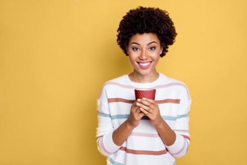 Uma mulher feliz com um suéter listrado azul vermelho rosa segurando uma xícara de café quente Café Pelé